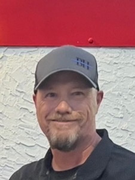 Jeremy Jenkins, smiling in a ball cap in front of a painted American flag